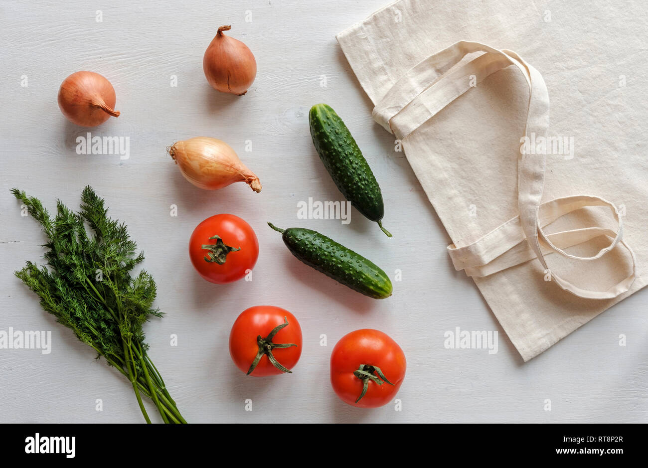 Stoff wieder verwendbare Einkaufstasche mit Lebensmitteln um einschließlich Tomaten, Zwiebeln, Gurken und Greens in einem flachen noch leben verstreut Stockfoto