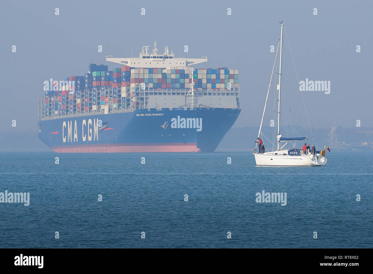 Das 400 Meter lange, Ultra-Large Container Ship, CMA CGM LOUIS BLERIOT, verlässt den Hafen von Southampton, EIN kleines Segelboot im Vordergrund. GROSSBRITANNIEN. Stockfoto