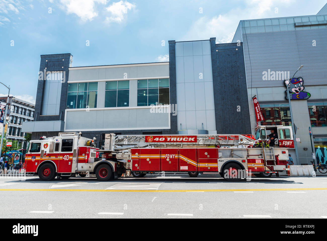 New York City, USA - 28. Juli 2018: Löschfahrzeug mit einer großen Leiter und ein Feuerwehrmann auf einer Straße mit Menschen in Harlem, New York City, USA geparkt Stockfoto