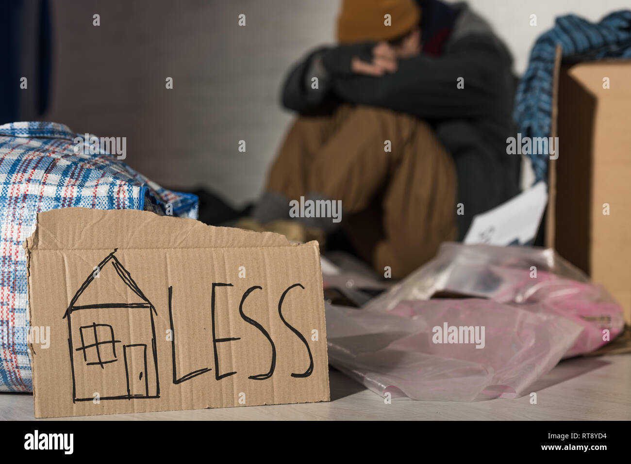 Selektiver Fokus der obdachlose Mann, den Kopf auf die Knie beim Sitzen auf der Müllkippe mit Karton Karte "Obdachlosen" Schriftzug Stockfoto