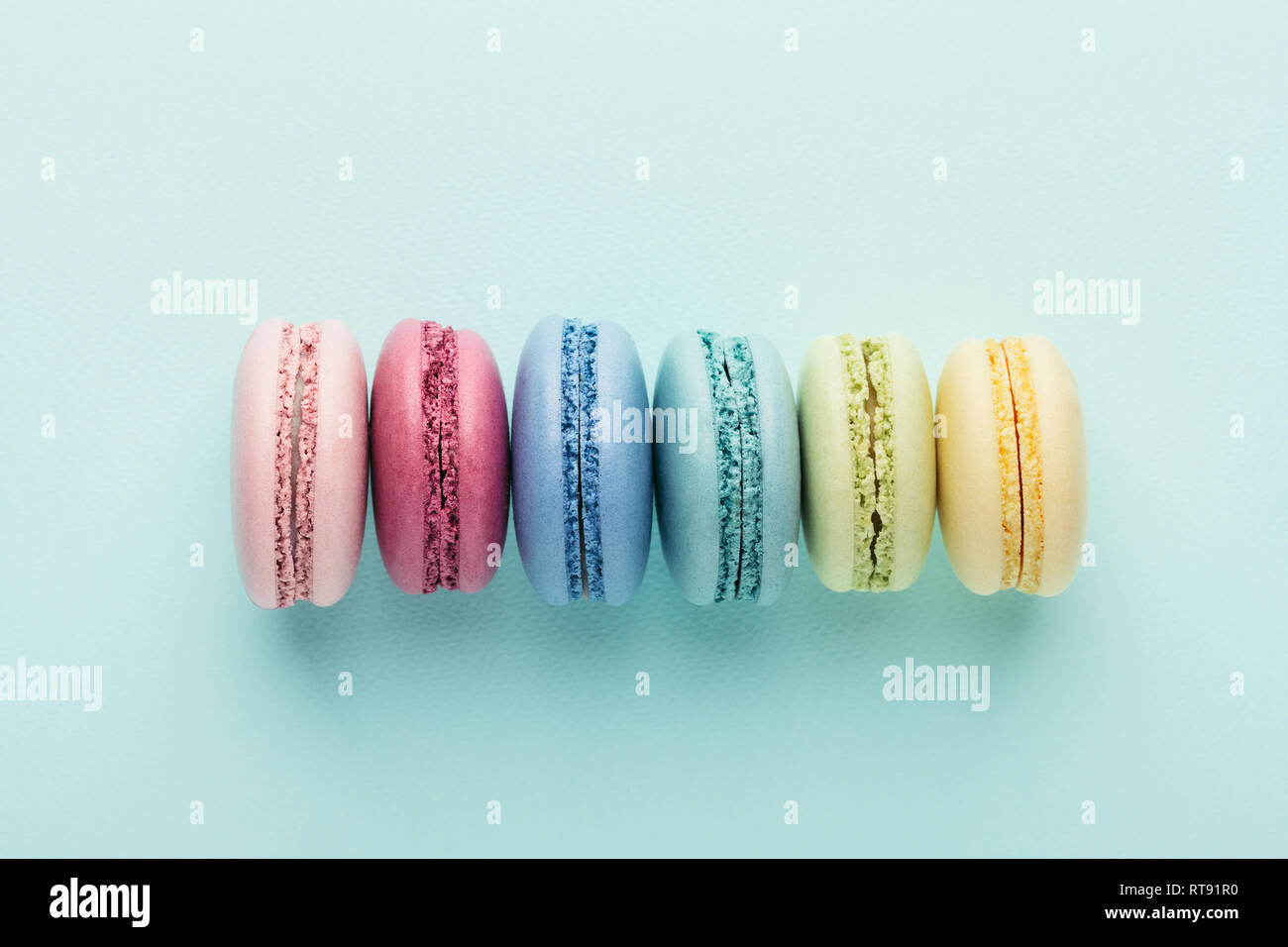 Reihe der bunte Macarons auf Türkisfarbenem Hintergrund. Ansicht von oben. Stockfoto