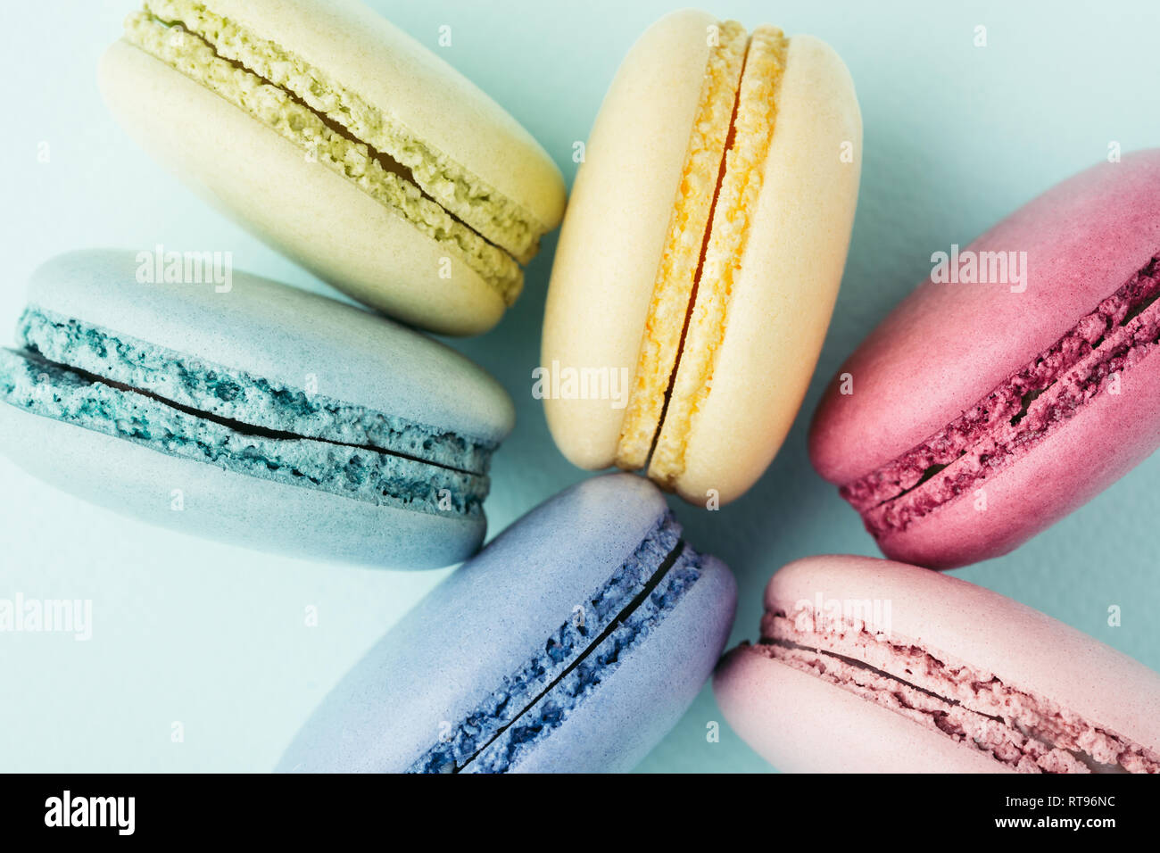 Reihe der bunte Macarons auf Türkisfarbenem Hintergrund. Ansicht von oben, aus der Nähe. Stockfoto