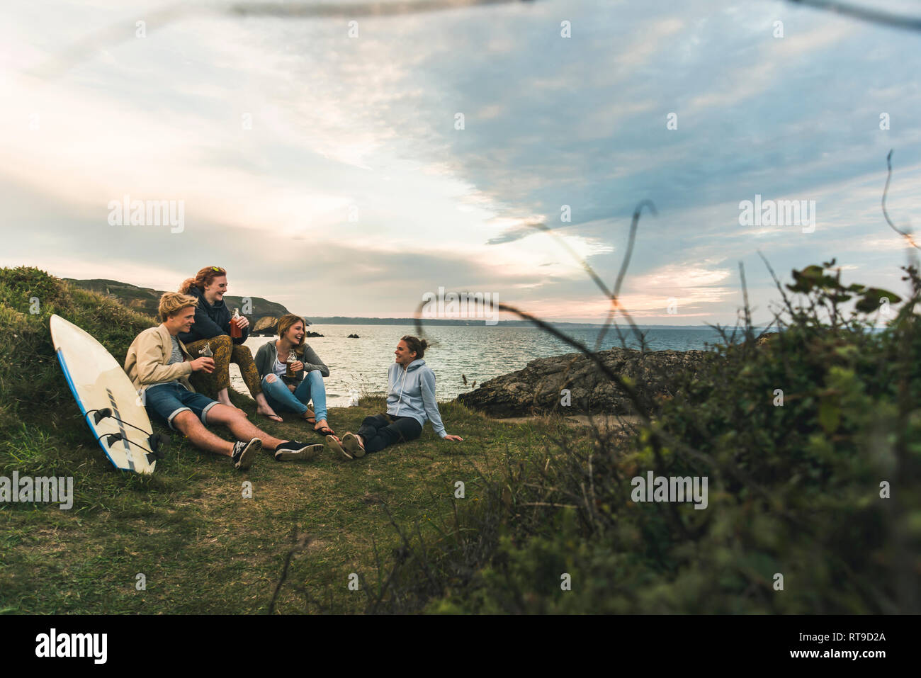 Gerne Freunde mit Surfbrett und Getränke Geselligkeit an der Küste bei Sonnenuntergang Stockfoto