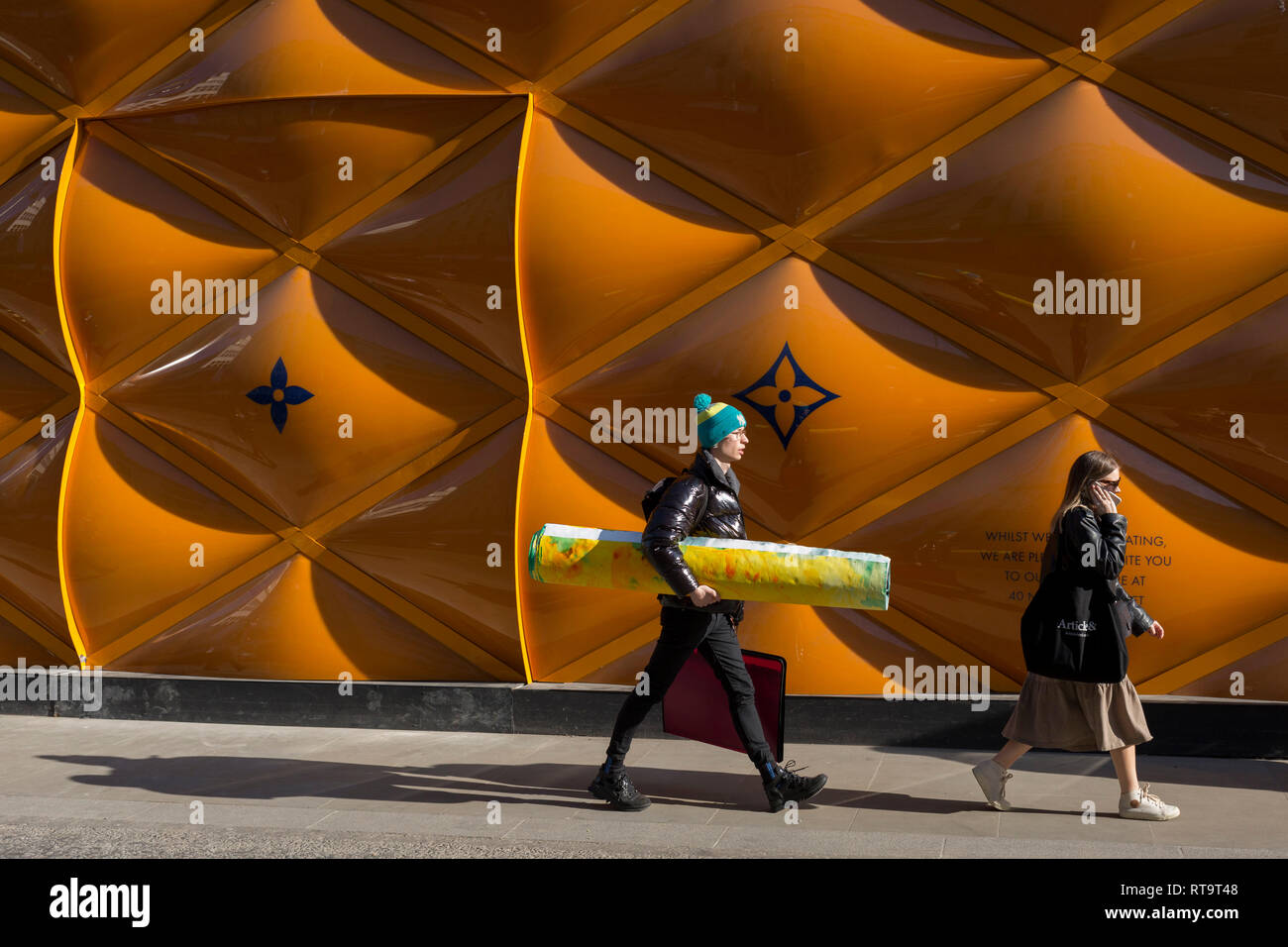Eine künstlerische Mann, der ein Kunstwerk unter dem Arm an der Temporären renovierung Horten der Luxusmarke Louis Vuitton in New Bond Street, am 27. Februar 2019 in London, England. Stockfoto