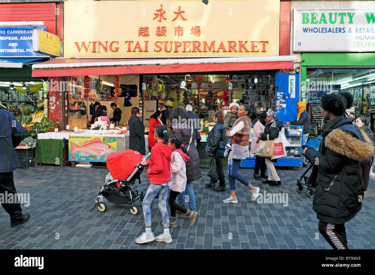 Käufer zu Fuß außerhalb Flügel Tai chinesischen Supermarkt Store & Brixton Street Market Electric Avenue Brixton London SW9 England UK KATHY DEWITT Stockfoto