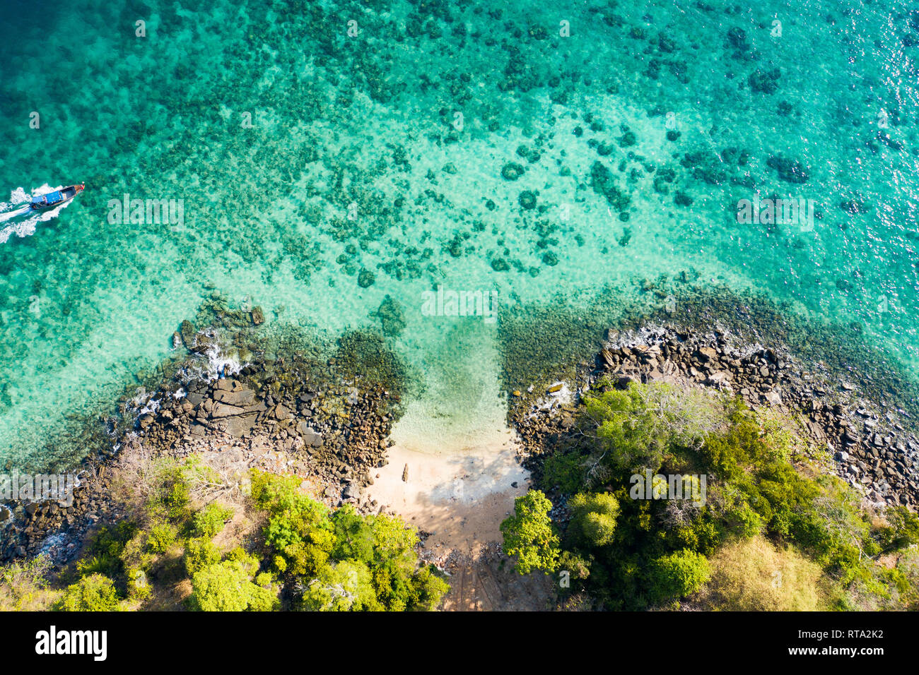 Ansicht von oben, Luftaufnahme eines traditionellen Long-tail-Boot segeln in der Nähe von einem atemberaubenden Korallenriff mit einer schönen kleinen Strand. Stockfoto