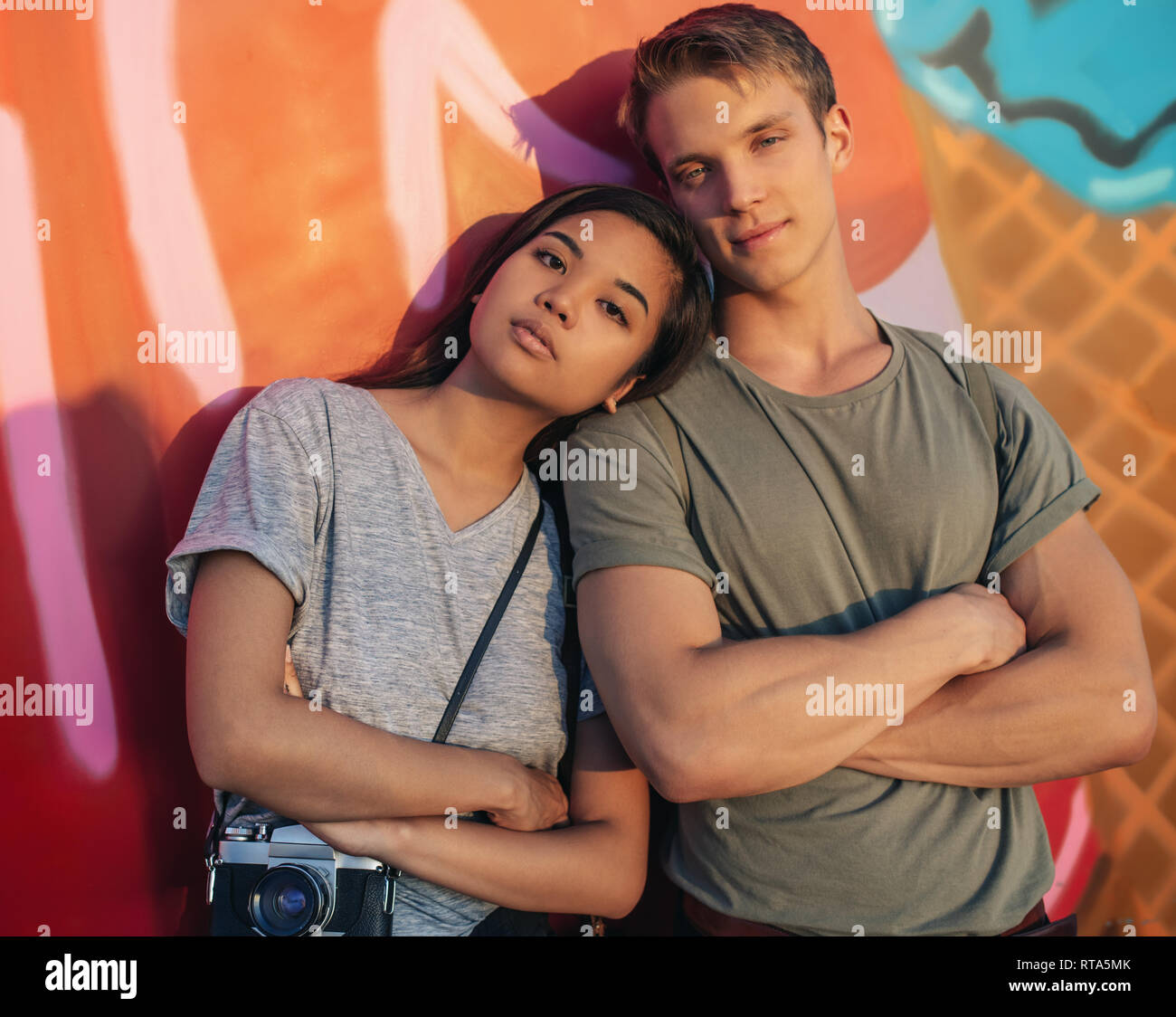 Junges Paar mit Haltung stehend durch eine Wand mit Graffiti Stockfoto
