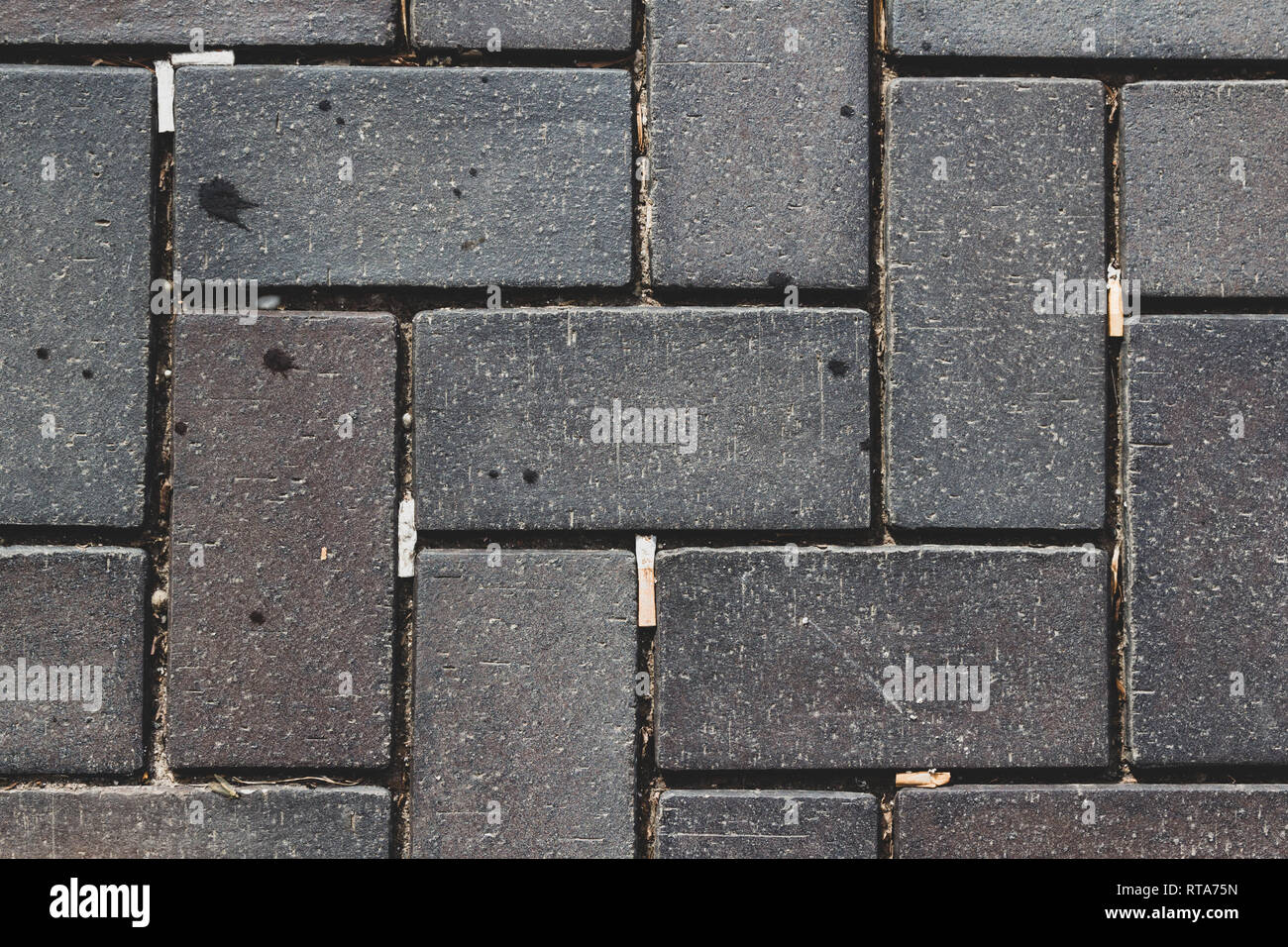 Kopfsteinpflaster und Zigarettenstummel in die Lücken geworfen. Kunststoff im Alltag die Verschmutzung auf der Straße. Stockfoto