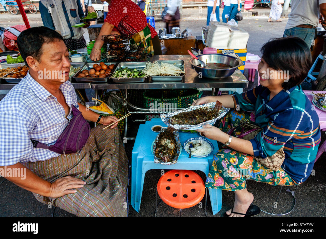 Ein älteres Ehepaar in traditioneller Kleidung Sitzen Essen Street Food, Yangon, Myanmar Stockfoto