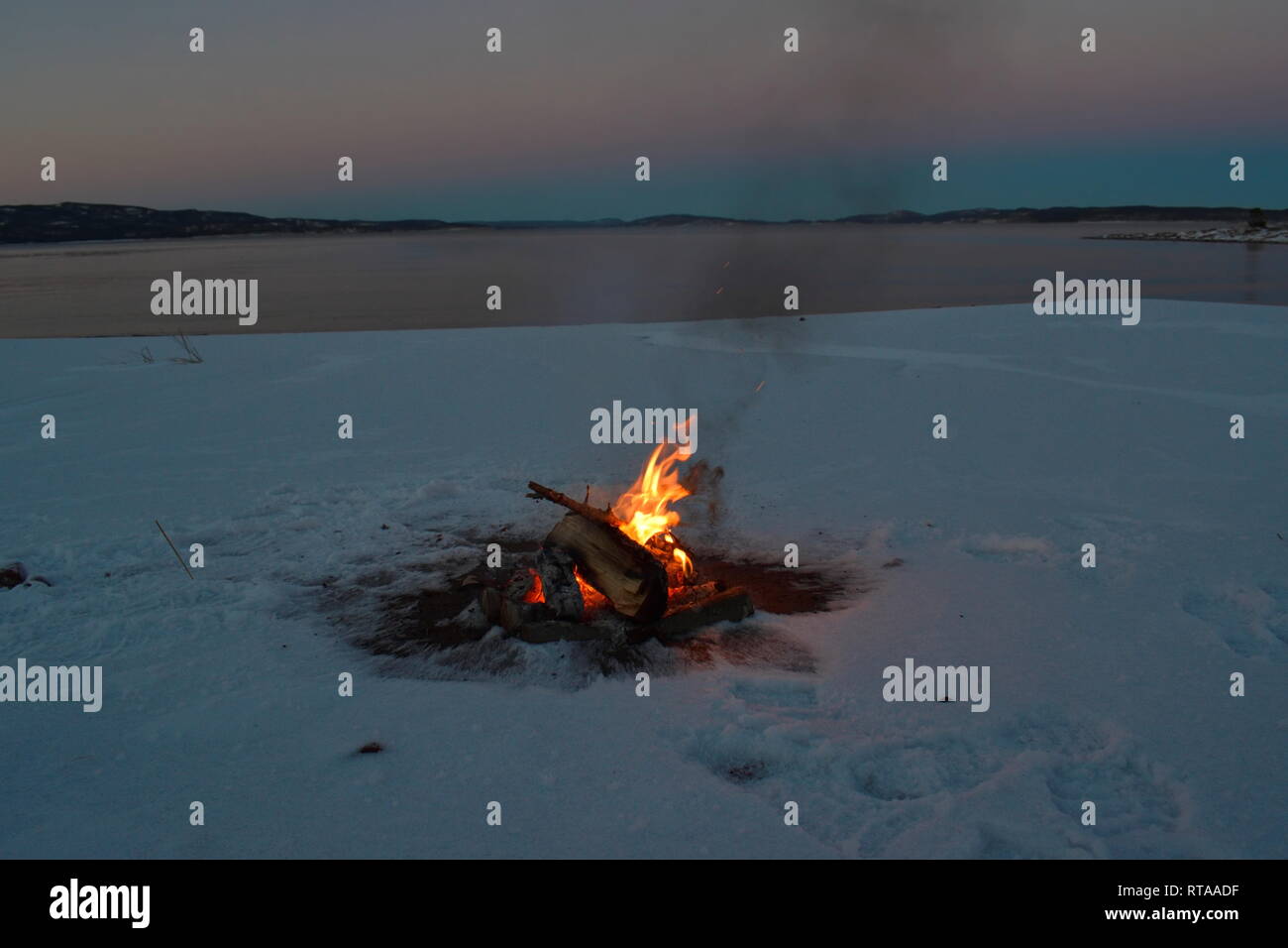 Ein Lagerfeuer brennt am Ufer einer Bucht der Ostsee. Es ist Sonnenuntergang an einem Wintertag, und der Strand ist mit Schnee bedeckt. Stockfoto