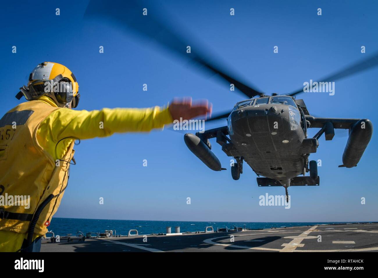 ARABIAN GULF (Feb. 4, 2019) Bootsmann Mate 1. Klasse Daniel Linsalata Signale Befehle an ein UH-60 Black Hawk Hubschrauber, zu Task Force Javelin zugeordnet, auf dem Flugdeck der Arleigh-Burke-Klasse geführte Anti-raketen-Zerstörer USS Mitscher (DDG57). Mitscher ist in die USA 5 Flotte Bereich der Maßnahmen zur Unterstützung der Marine im Einsatz für die Stabilität und Sicherheit in der Region zu gewährleisten und verbindet das Mittelmeer und den Pazifischen Raum durch den westlichen Indischen Ozean und drei strategischen Punkten ersticken. Stockfoto