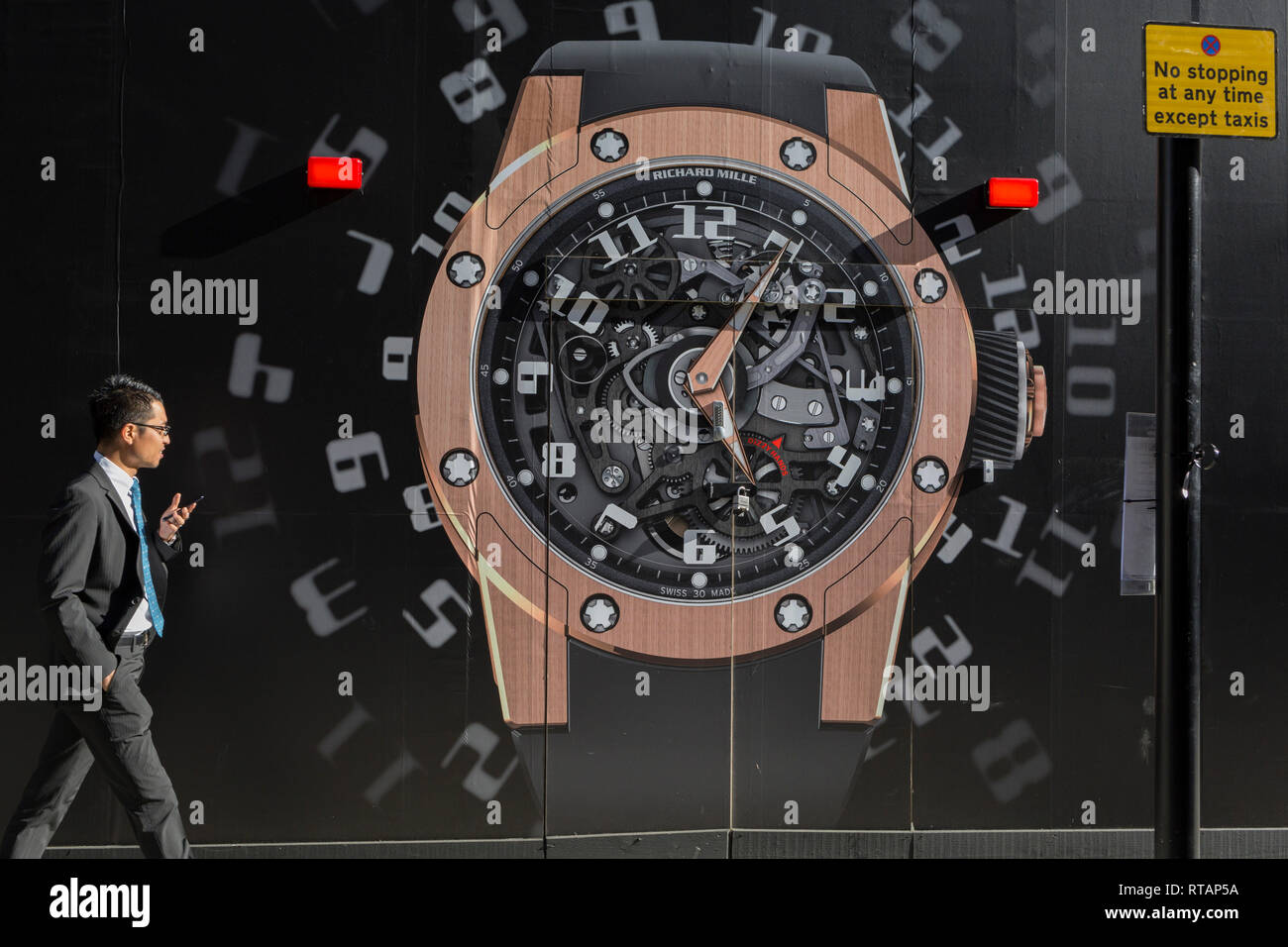 Ein Geschäftsmann Wanderungen vorbei an einem Bau das Horten von einer Uhr außerhalb der neuen Richard Mille shop in New Bond Street, am 25. Februar 2019 in London, England. Stockfoto