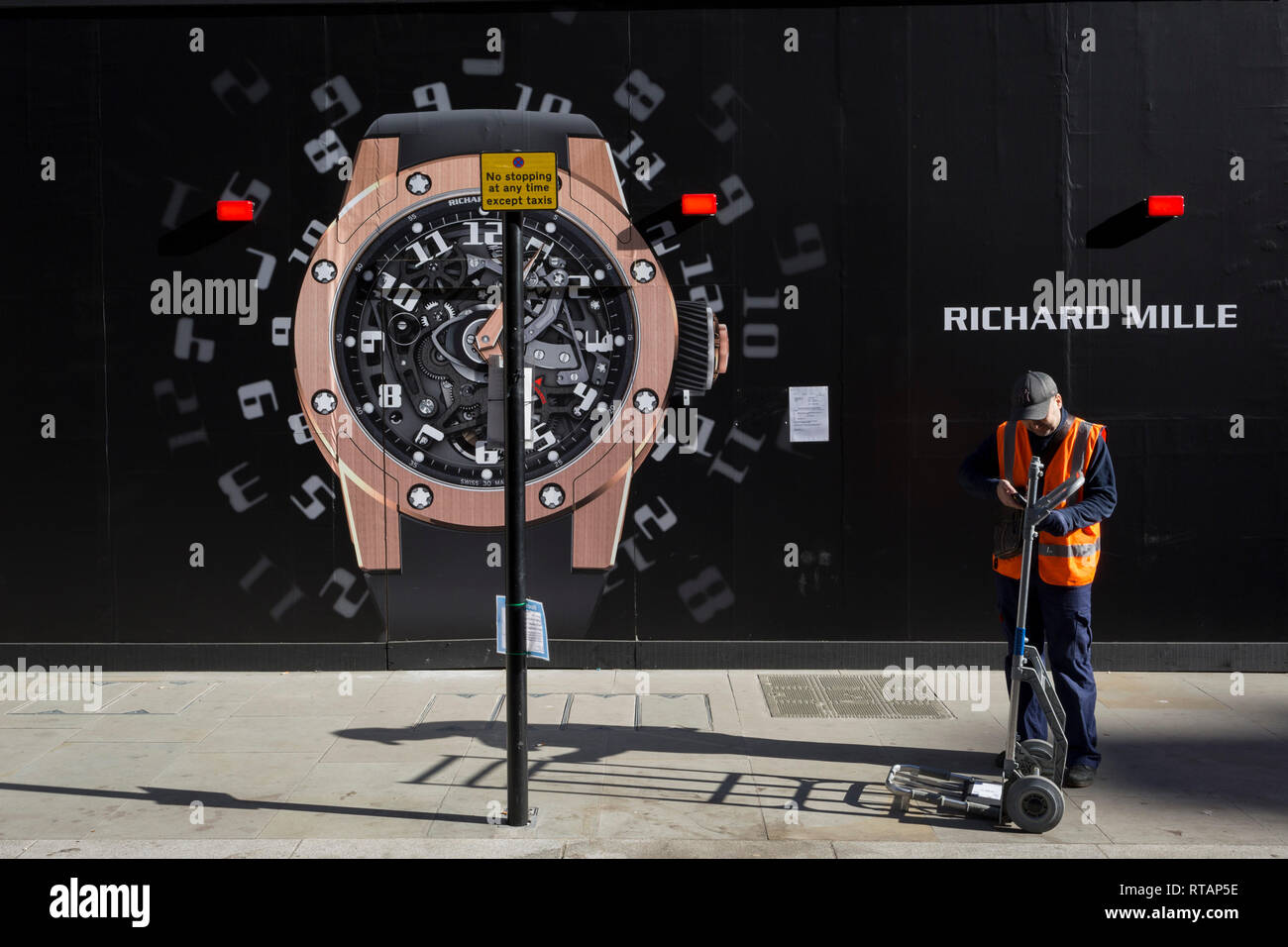 Ein Kurier prüft seine Lieferung Gerät neben einem Bau das Horten von einer Uhr außerhalb der neuen Richard Mille shop in New Bond Street, am 25. Februar 2019 in London, England. Stockfoto