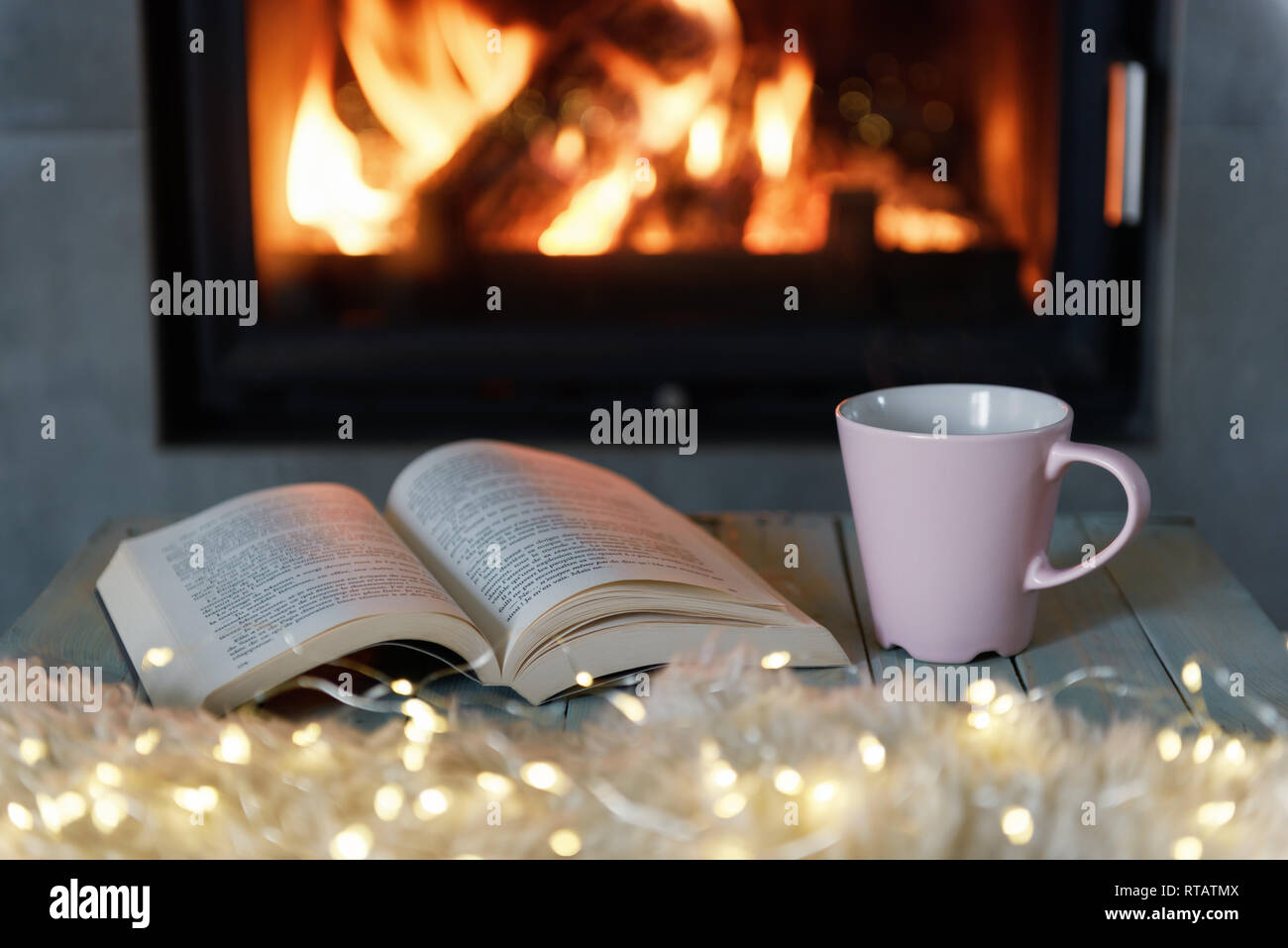 Buch und einer Tasse Tee in der Nähe von brennenden Kamin. Hygge Konzept Stockfoto