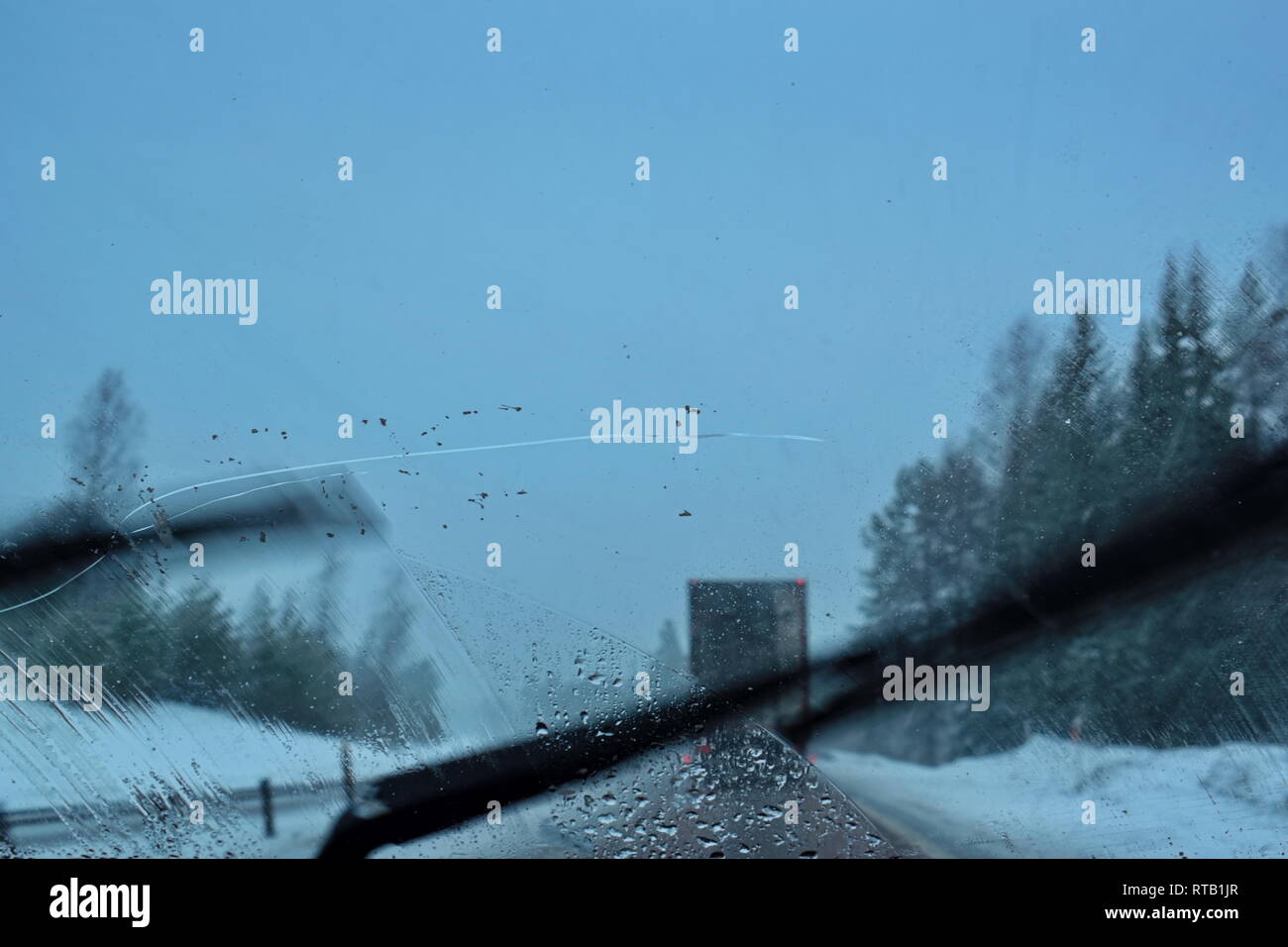 Pov-shot durch die Windschutzscheibe eines Autos fahren auf einen Motor Weg durch verschneite Wälder in der Abenddämmerung. Die Scheibenwischer arbeiten, Schaben über die Tiefen cr Stockfoto