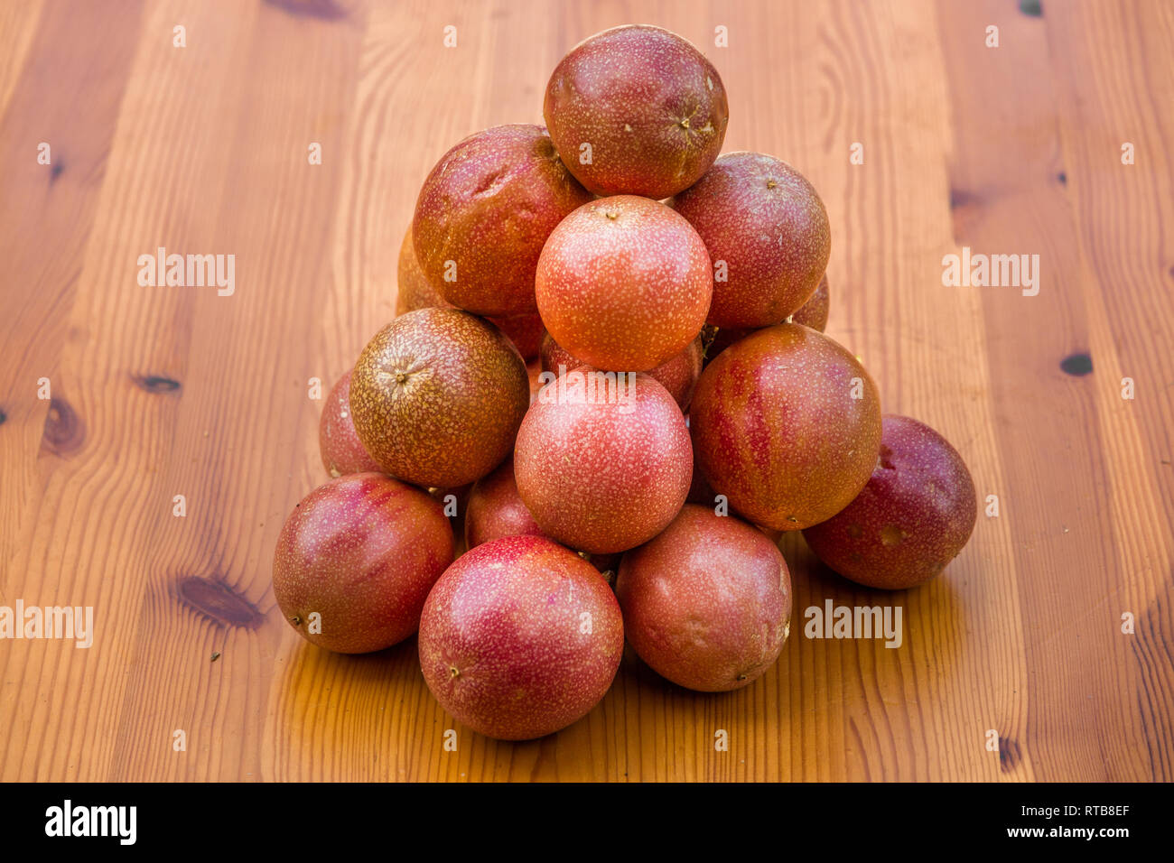 Mehrere schöne rote Leidenschaft Früchte (Passiflora edulis), gerupft und übereinander auf einen hölzernen Tisch gestapelt. Stockfoto