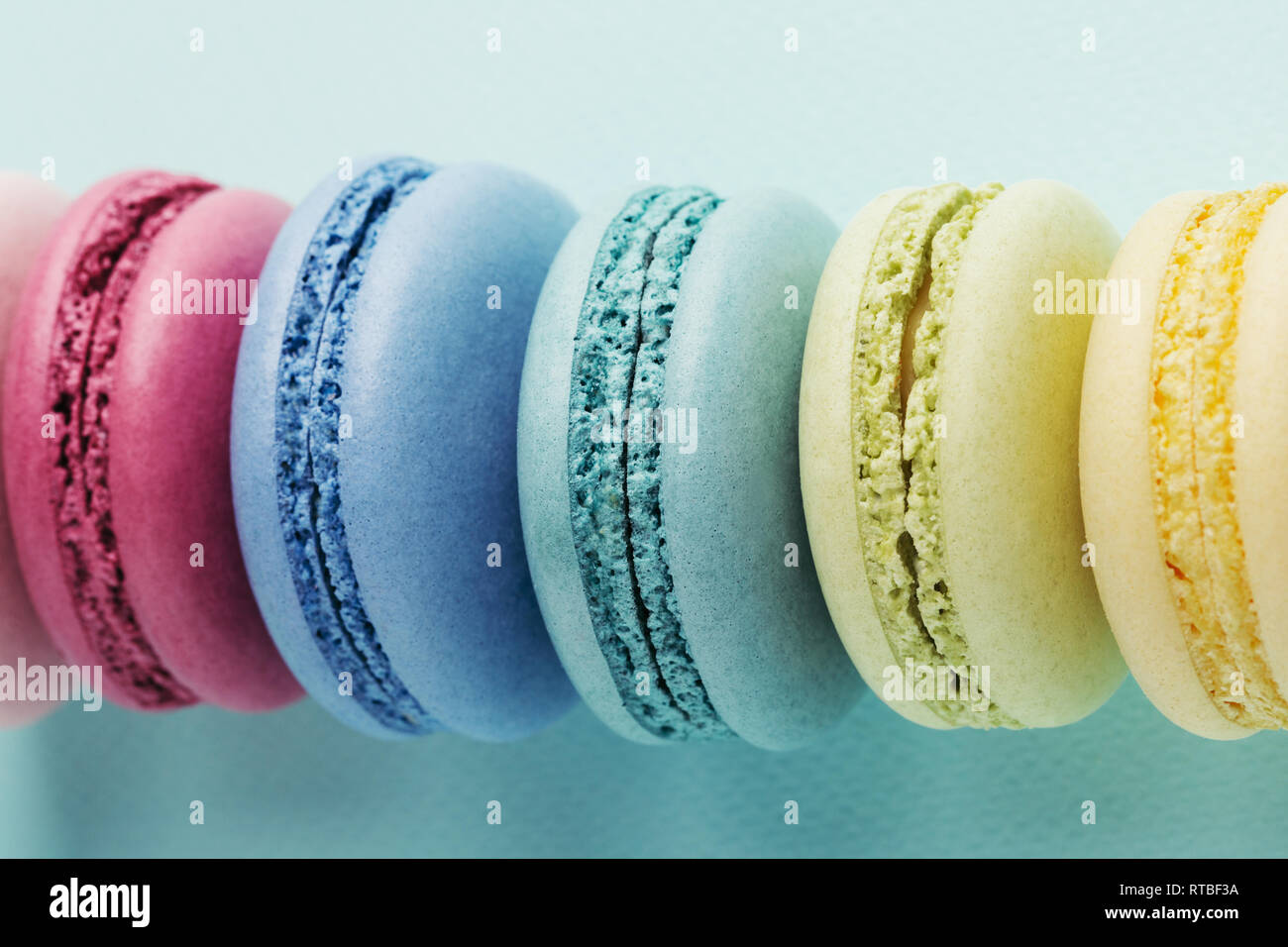 Reihe der bunte Macarons auf Türkisfarbenem Hintergrund. Ansicht von oben, aus der Nähe. Stockfoto