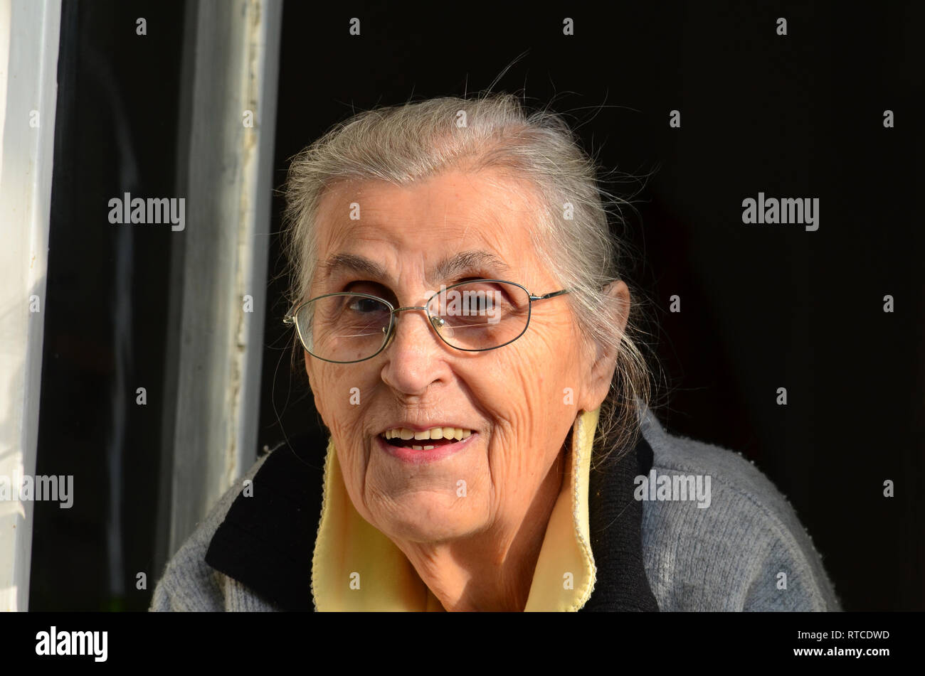 Porträt der fröhliche, gesunde alte Dame mit Brille schauen durch Fenster Stockfoto