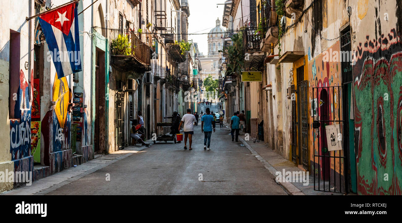 Havanna, Kuba - vom 25. Juli 2018: Blick auf eine Straße in der Altstadt von Havanna mit Menschen zu Fuß, das Capitol Gebäude in Aussicht, eine kubanische Flagge und Graffiti an den Wänden. Stockfoto