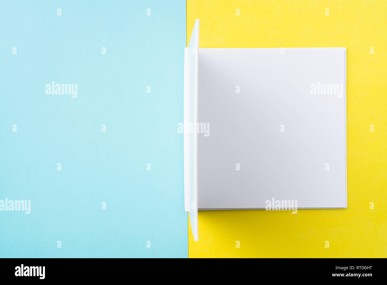 Designkonzept - Ansicht von oben öffnen Quadratische weiße Notebook auf bunten gelber und blauer Hintergrund für Modell der Serie 7. Stockfoto