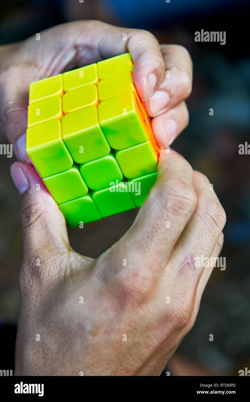 Nahaufnahme eines asiatischen Neon farbigen Nachbau eines Rubik's Cube, der von zwei Händen einer echten Person gehalten Stockfoto