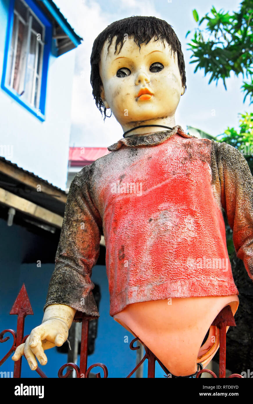Eine schmutzige bunten Kunststoff Puppe ohne Beine auf einen Gartenzaun eingeklemmt wird. Das ist ein Blickwinkel - Mit einem Haus im Hintergrund, in den Philippinen gesehen Stockfoto