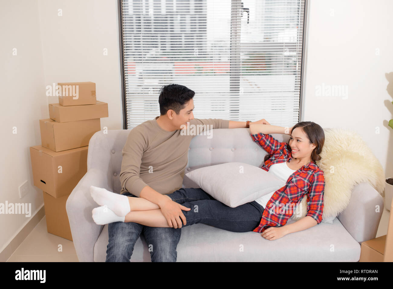 Glückliches Paar entspannt auf einem Sofa, das Spaß am Umzugstag, neugierige junge Hausbesitzer genießen Umzug in ein neues Zuhause, positive lachenden Mann und Frau Stockfoto