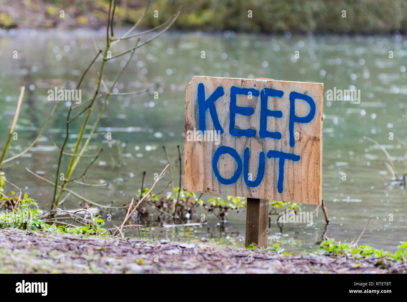 Halten Sie sich abmelden Hand geschrieben auf ein hölzernes Schild in den Boden durch einen See stecken. Stockfoto