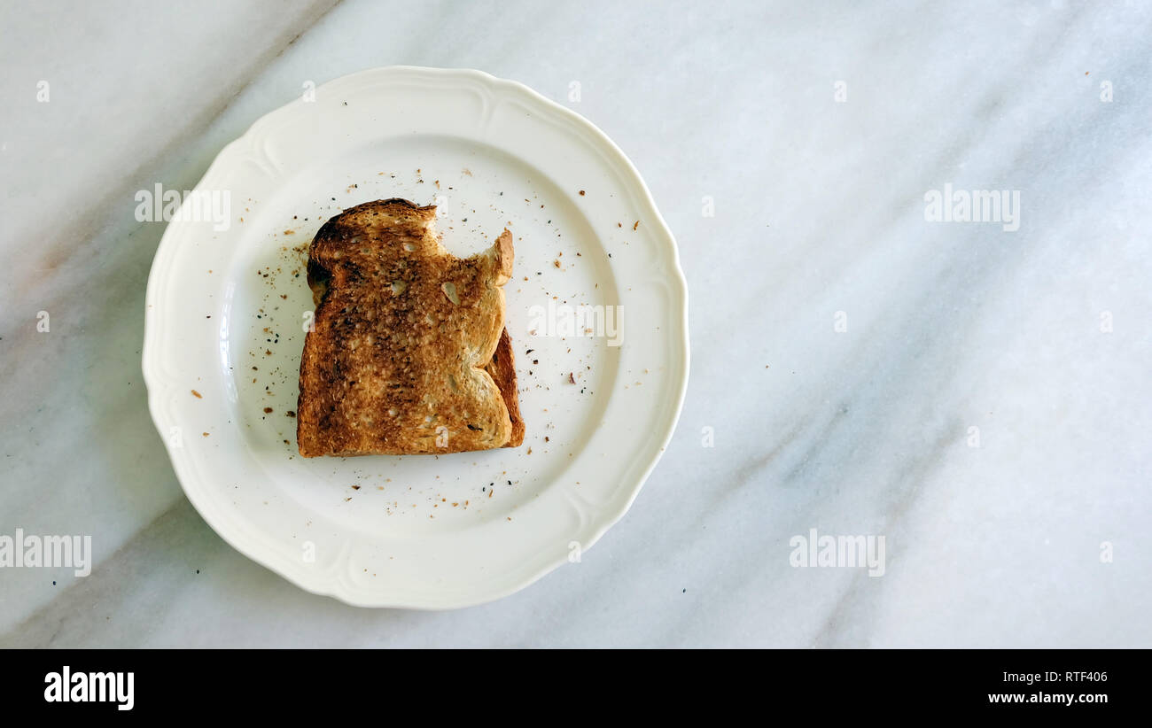 Toast Brot gebissen Sie an der oberen Ecke, auf einem weißen Teller mit Krümel herum, auf Marmor. Stockfoto