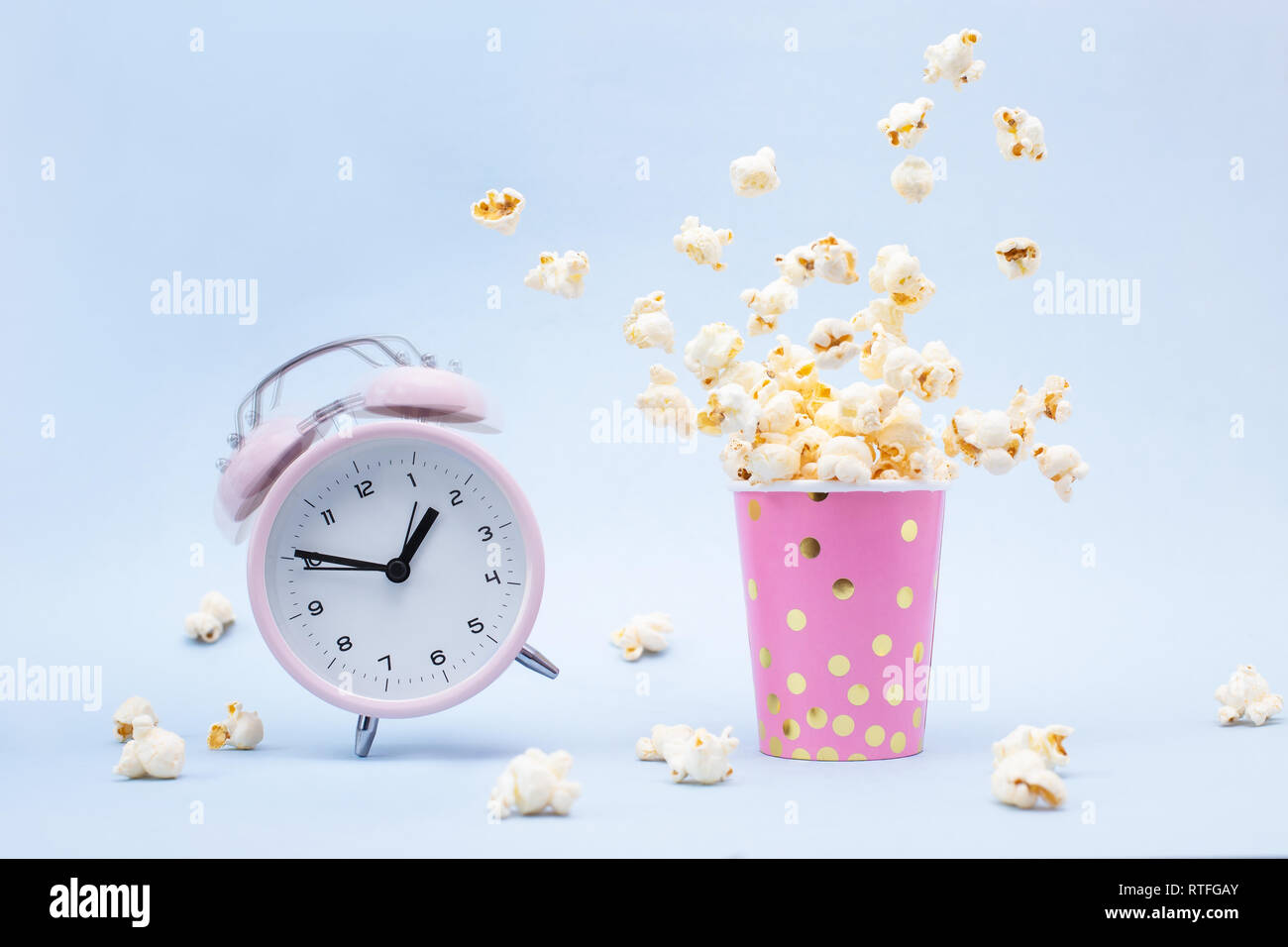 Flying Popcorn in einem hellen Glas und ein Klingelnder Wecker auf blauem Hintergrund. Zeit für einen Spaß-Konzept. Stockfoto