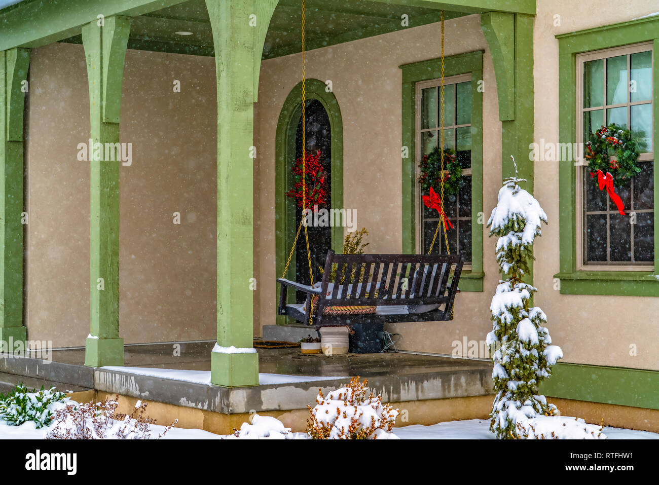 Haus mit Hollywoodschaukel und einladende Kränze. Veranda eines Hauses in Götterdämmerung, Utah mit einer Schaukel und nassen Boden aus geschmolzenem Schnee. Einladende Kränze ca Stockfoto