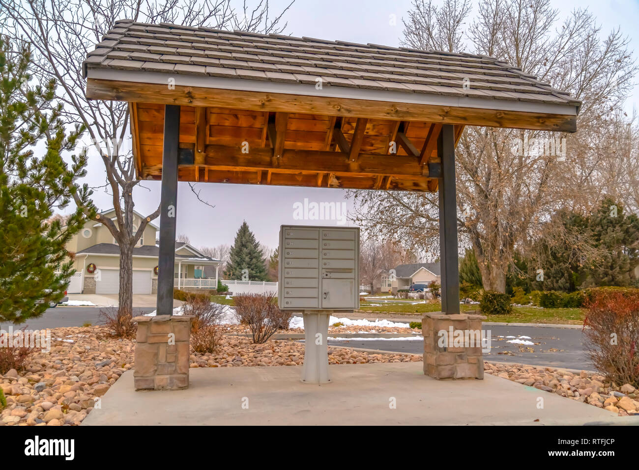 Outdoor cluster Mailbox unter einem Bürgersteig werfen. Ein Außenpool Mailbox unter einem bürgersteig Schuppen mit Häusern und Bäumen im Hintergrund. Nummerierten Fächer Stockfoto