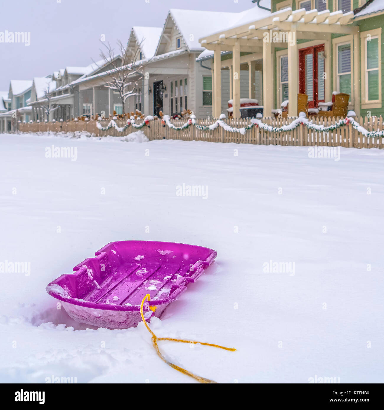 Lebendige lila Schlitten mit Schnee und Wohnungen Hintergrund. Nahaufnahme  einer lebendigen lila Schlitten auf einem Bett von frischem Schnee. Häuser  mit hölzernen Zaun und verschneiten r Stockfotografie - Alamy
