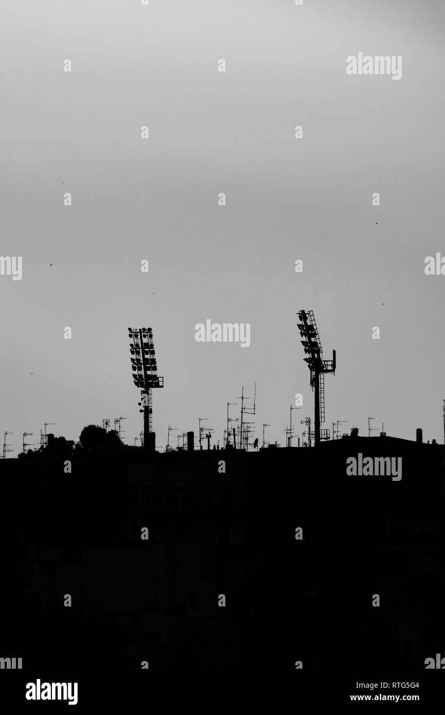 Silhouetten der beiden Sport Stadion leuchtet bei Sonnenuntergang, Altstadt von Matera, Basilikata, Süditalien. Schwarz-weiss Bild, darunter einige der städtischen Gebäude und Dächer Stockfoto