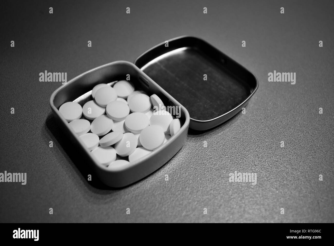 Pillen in Metallbehälter auf Grau, Schwarz und Weiß Stockfoto