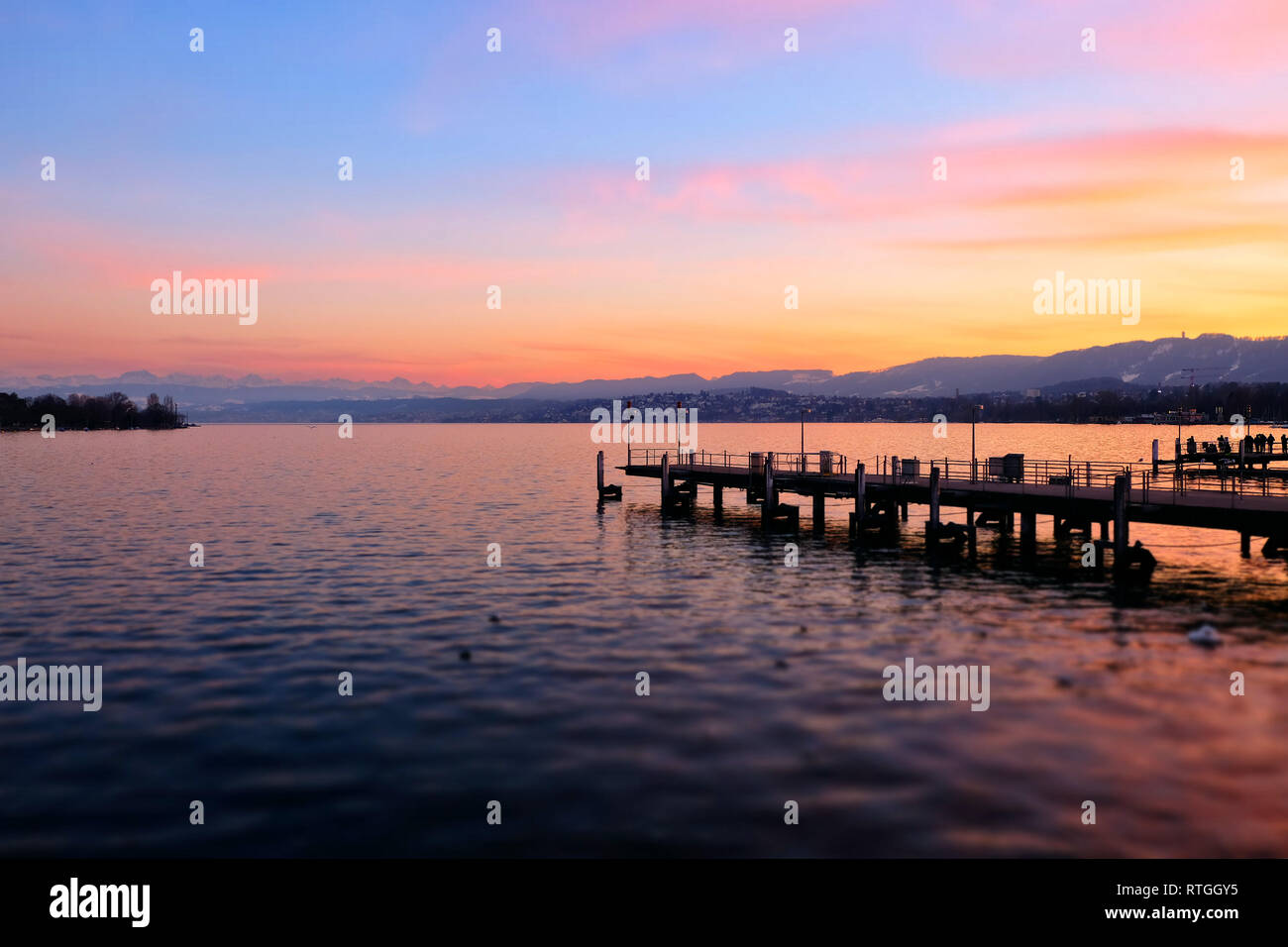 Blick Ÿber den ZŸrichsee bei Sonnenuntergang mit Bootsanleger in die schneebedeckten Schweizer Alpen. Stockfoto