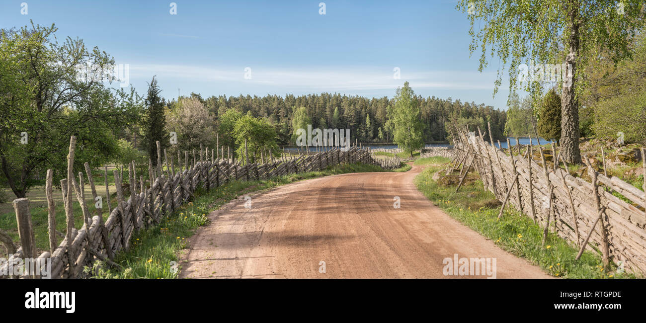 Malerisches Land Straße, die zu einem See durch eine wunderschöne Landschaft mit roundpole Zäune, Smaland, Schweden, Skandinavien. Stockfoto
