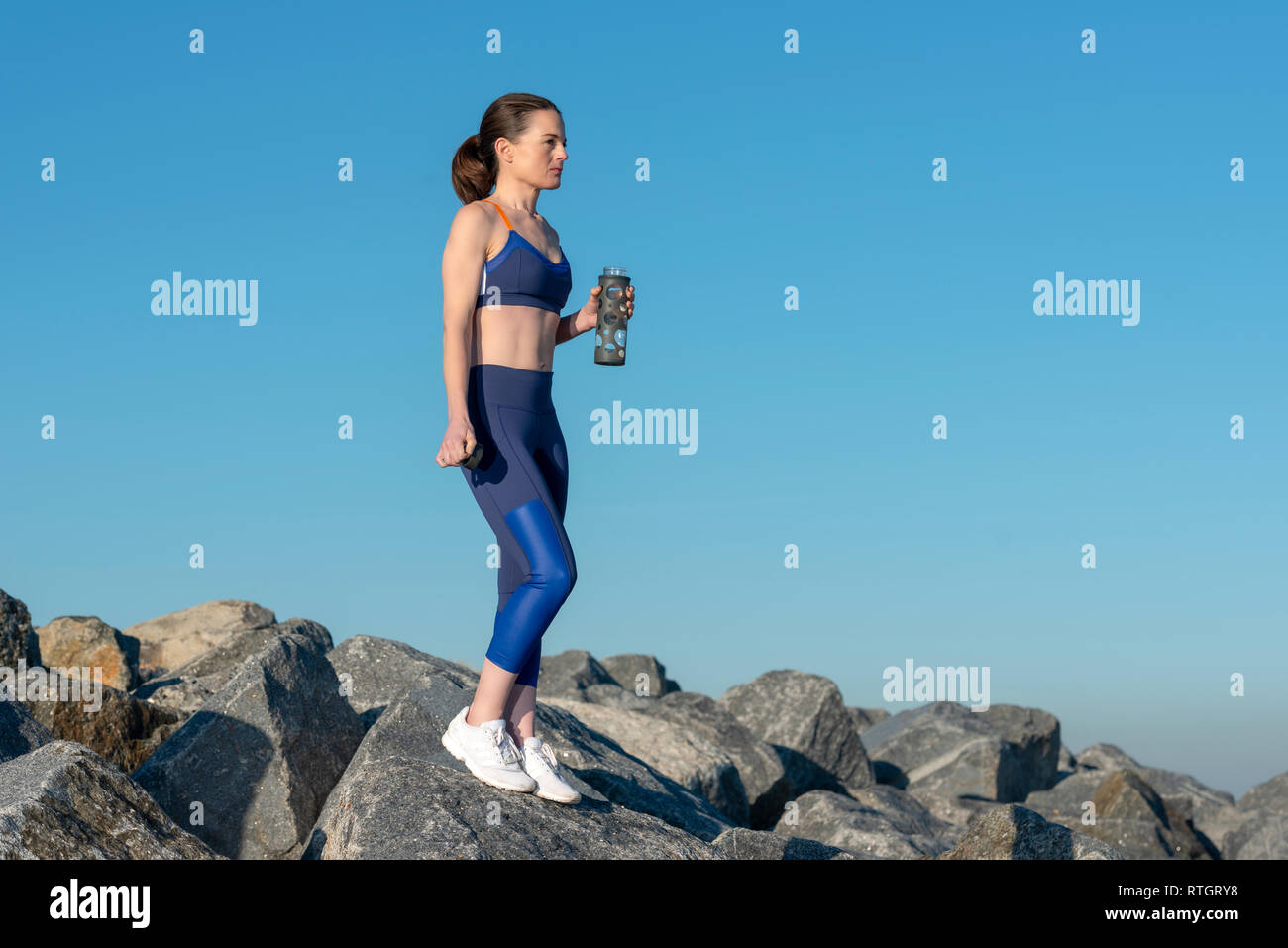 Frau steht auf Felsen mit einem Glas sport Trinkflasche Stockfoto