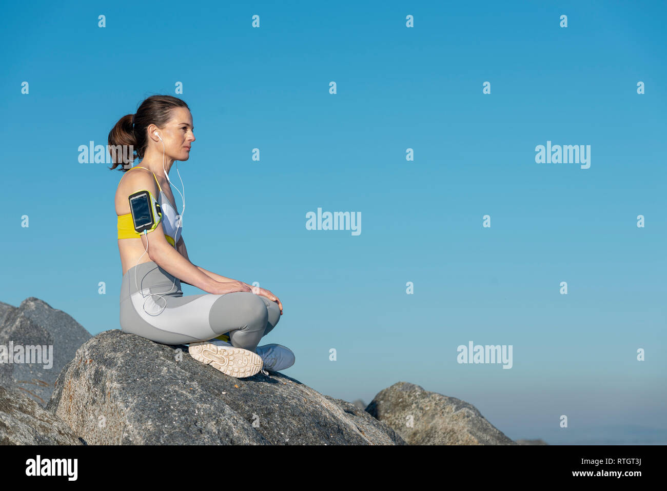 Frau Sportswear sitzen auf den Felsen Ausruhen nach übung Hören von Musik auf Ihrem Smartphone Stockfoto