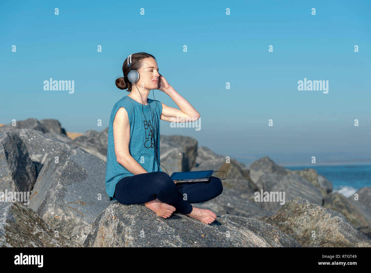 Frau sitzen auf den Felsen am Meer Musik auf Ihrem Tablet mit Kopfhörern Stockfoto