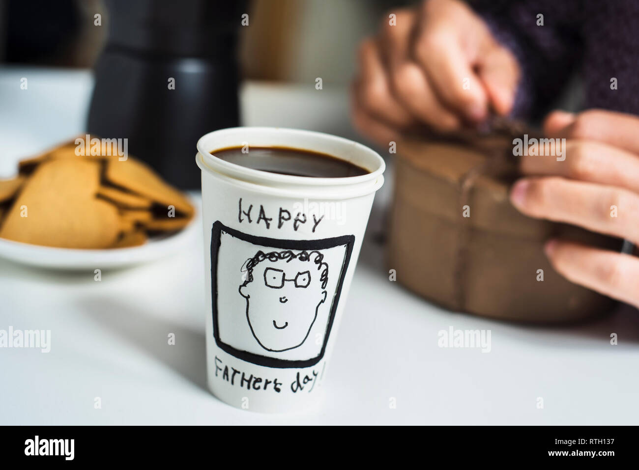 Nahaufnahme von einem verwerfbaren Tasse mit Kaffee, mit dem Text happy Vatertag handschriftlich auf einem Tisch für Frühstück und einer weißen Mann öffnen Stockfoto