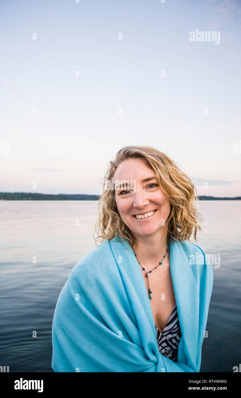 Eine lächelnde Frau am Rande von einem Körper von Wasser in der Abenddämmerung. Stockfoto