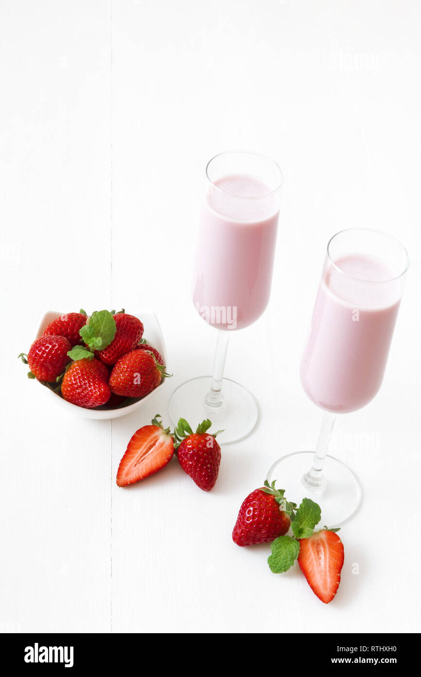 Strawberry Smoothie. 2 Gläser Erdbeer Milchshake, Porzellan Schüssel mit Erdbeeren verziert mit wenigen echten Erdbeeren und frischer Minze. Weiß Stockfoto