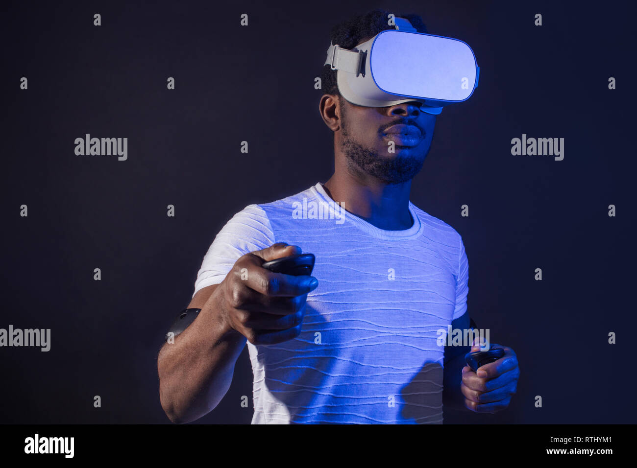 Dunkelhäutige männliche tourisistic Ventilator 3D-Tour nach Asien, stehend mit Head Mounted Display und Handheld Controller auf dunklem Hintergrund mit Rot Blau Stockfoto