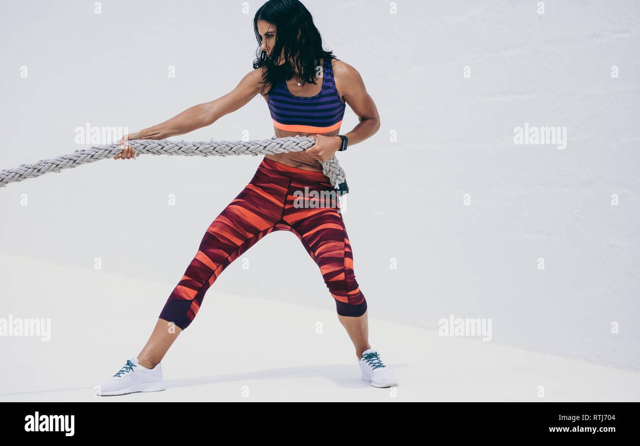 Fitnesstraining-Frau mit einem Kampfseil. Seitenansicht einer athletischen Frau beim Krafttraining durch Ziehen eines Kampfseils. Stockfoto