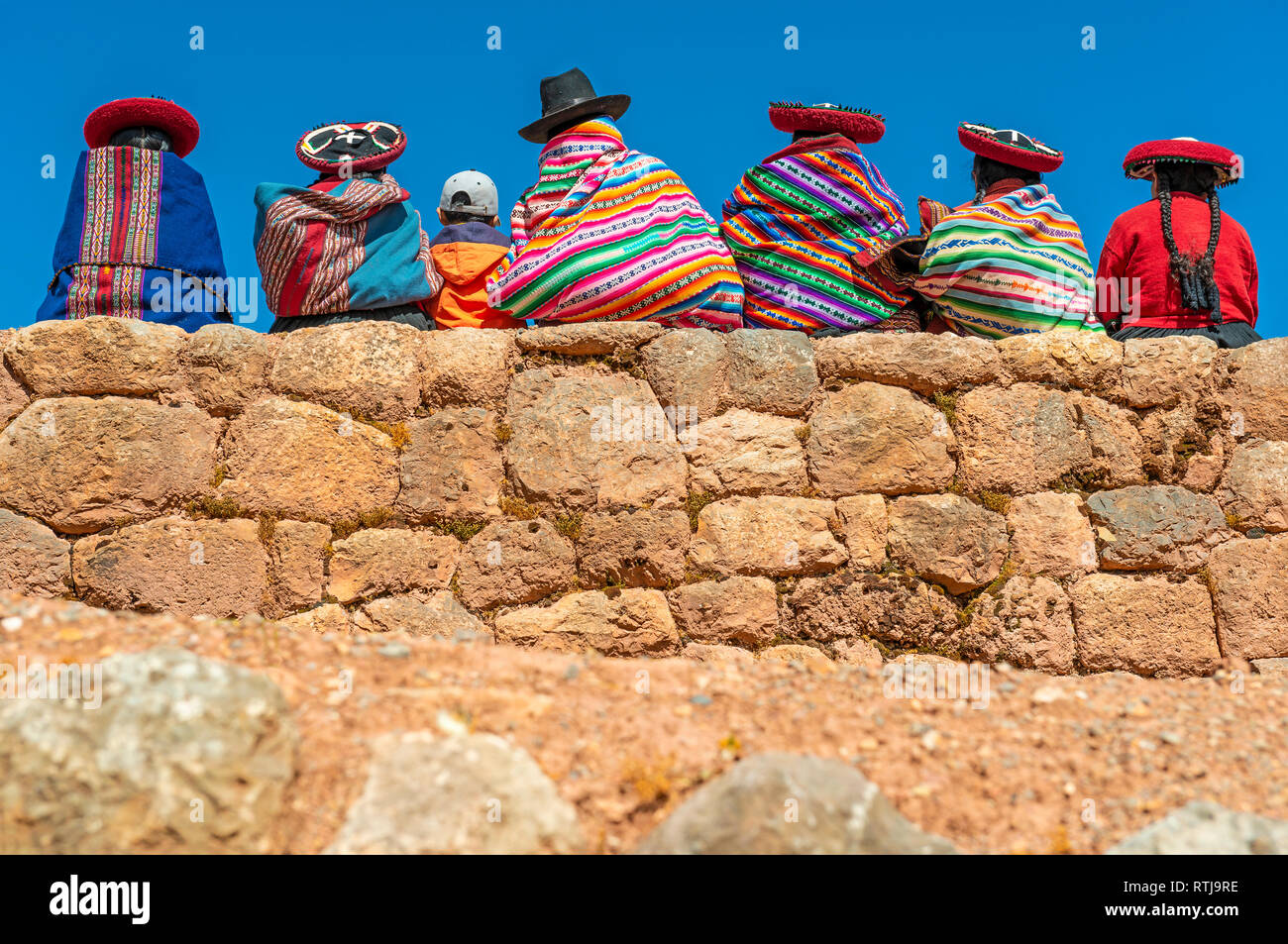 Eine Gruppe von Quechua indigenen Frauen in traditioneller Kleidung mit einem Jungen auf einer alten Inka-Mauer sitzen, Chinchero, Cusco, Peru. Stockfoto