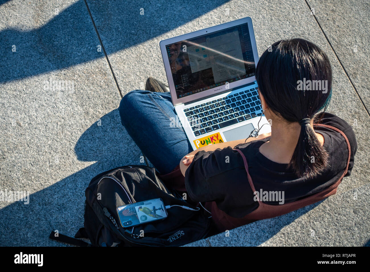 Bild von oben der jungen Dame sitzen draußen in der Sonne und mit Ihrem Laptop und Handy an Kohle Tropfen Yard, Kings Cross, London, England Stockfoto