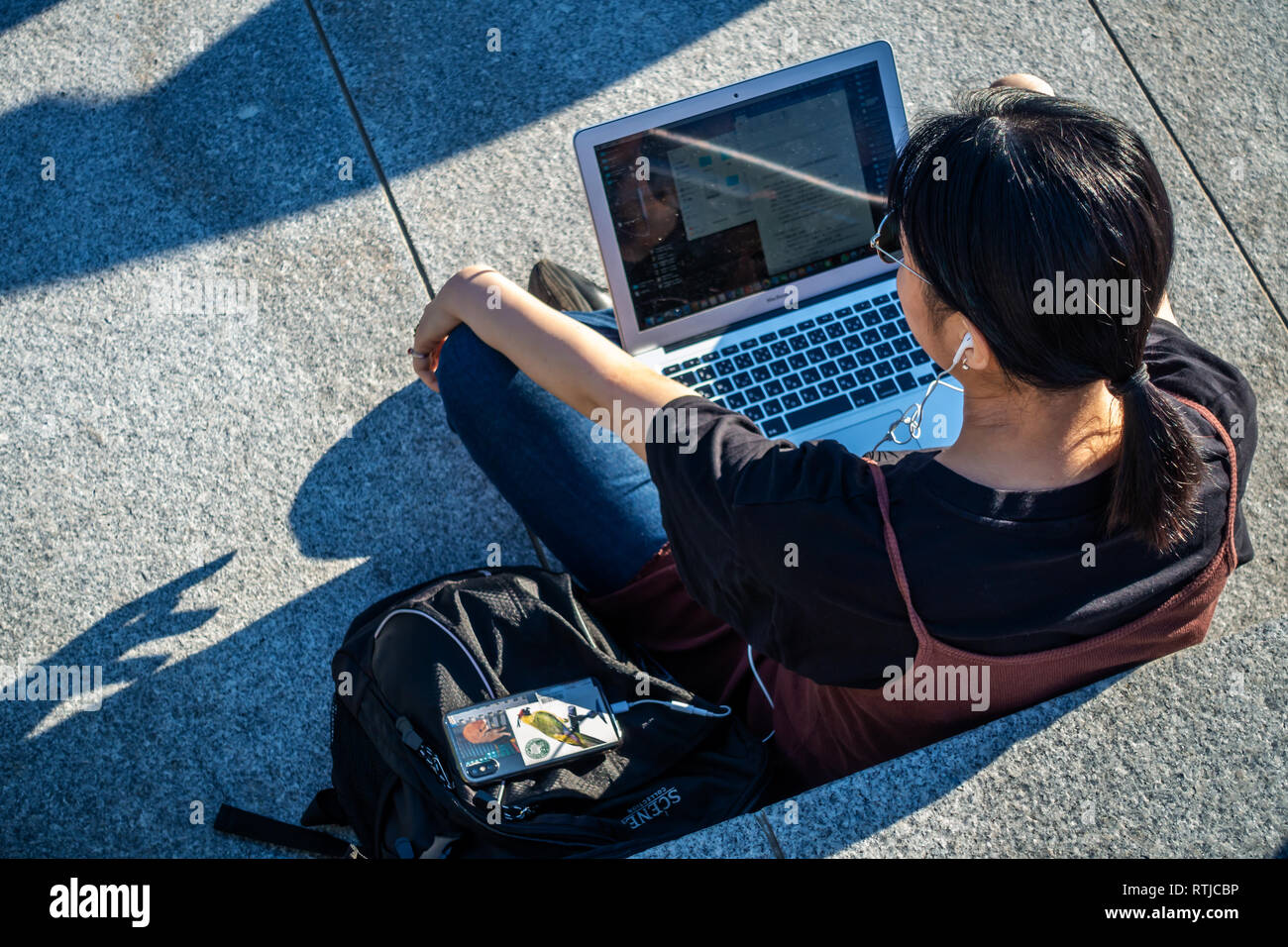 Bild von oben der jungen Dame sitzen draußen in der Sonne und mit Ihrem Laptop und Handy an Kohle Tropfen Yard, Kings Cross, London, England Stockfoto