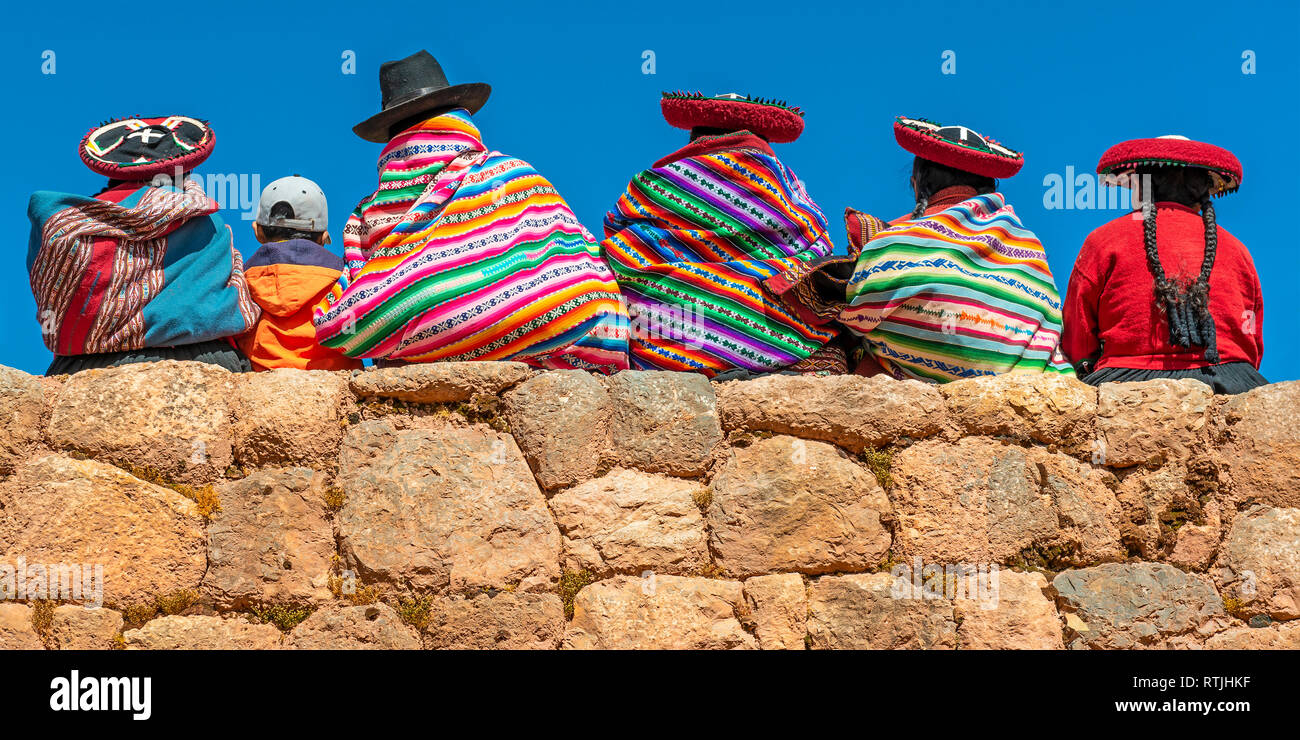 Peruanische Quechua Ureinwohner mit traditionellen Textilien, Hüten und Frisuren an einer Inka-Wand in Chinchero, Cusco, Peru. Stockfoto