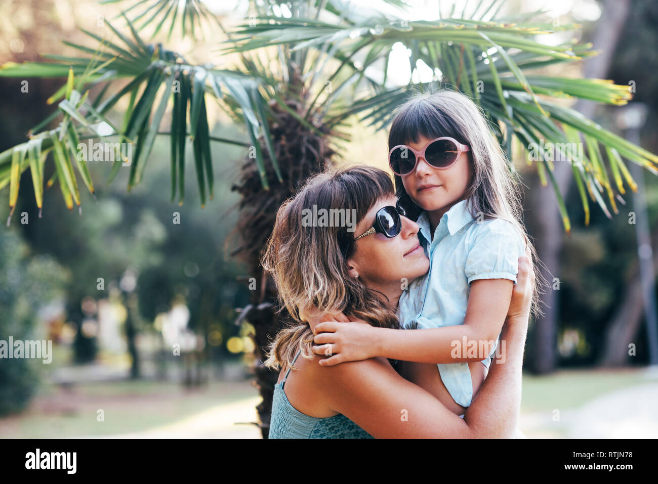 Mutter und Tochter in der Sonnenbrille halten einander vor dem Hintergrund der Palmen. Stockfoto